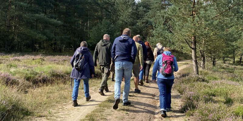 Foto van deelnemers van de excursie Wolf en Spoor van Werkgroep Wolf Nederland, ze wandelen over een onverhard pad in de natuur.